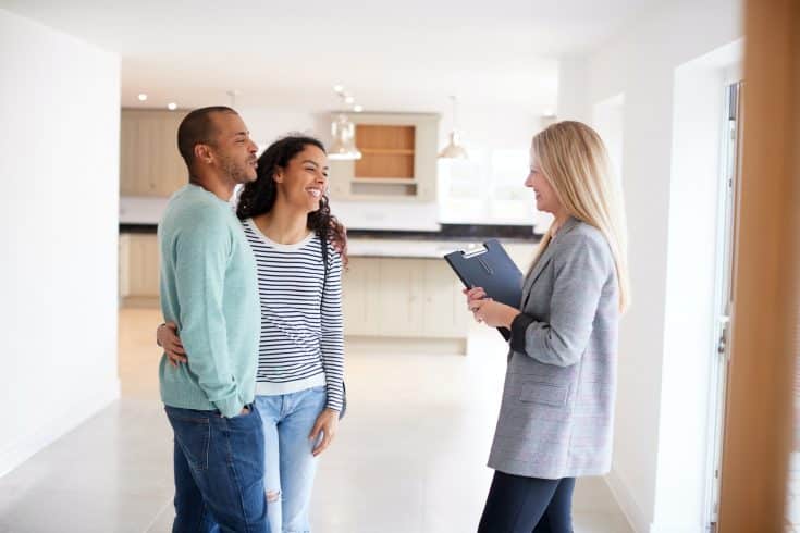 Female Realtor Showing Couple Interested In Buying Around House
