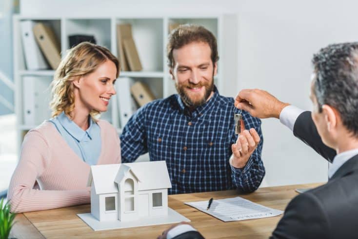 portrait of happy couple getting keys from new home from realtor in office
